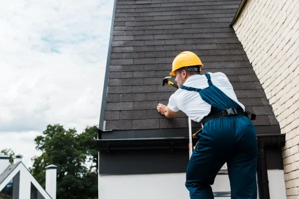 A repairman in uniform and helmet repairing the roof.